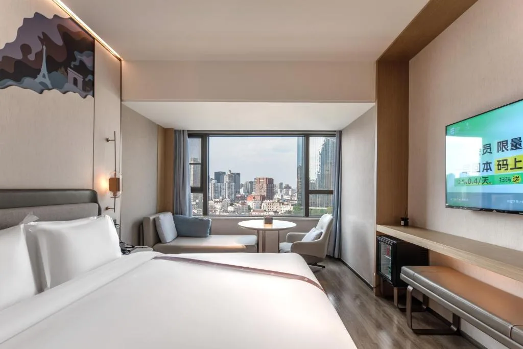 Modern city hotel room with king bed and seating nook by window overlooking skyline, quiet off-season stay