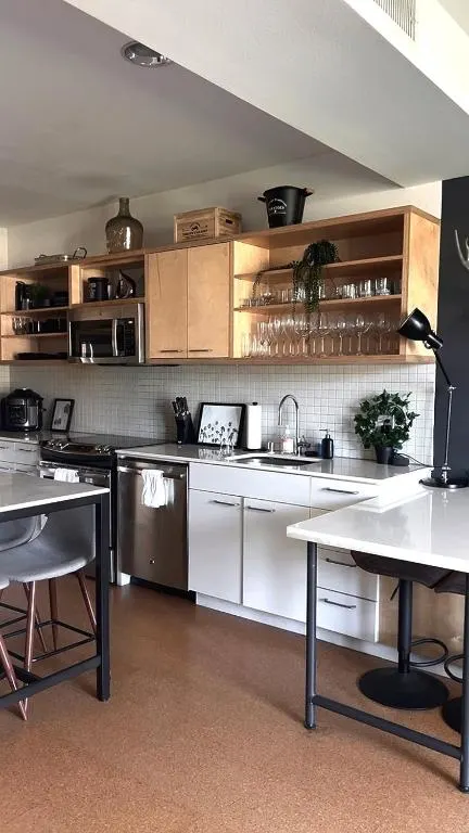 Empty modern kitchenette with white counters, wood shelving and stools in a cozy off-season rental.