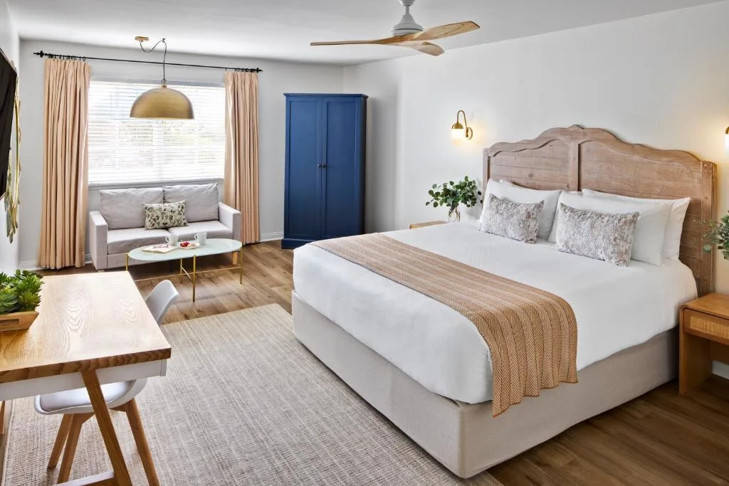 Bright modern hotel suite with king bed, wood accents and sofa, quiet off-season retreat atmosphere.
