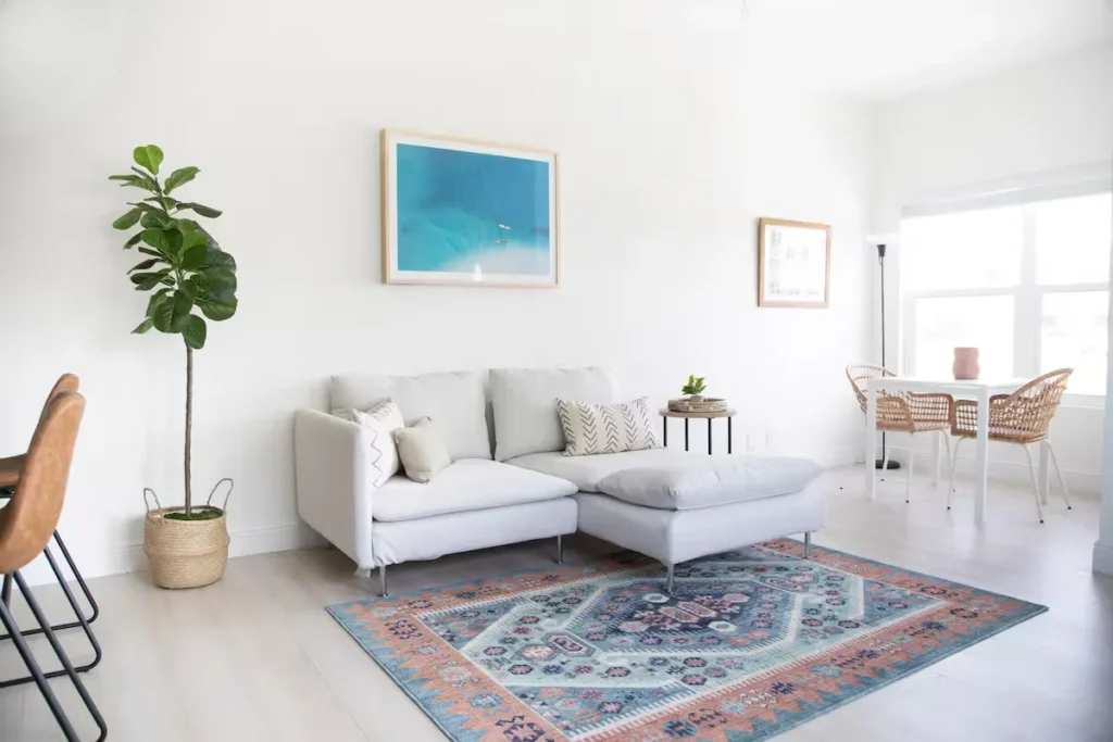 Bright vacation rental living room with white sectional, colorful rug and sunlit wicker dining set in off-season calm