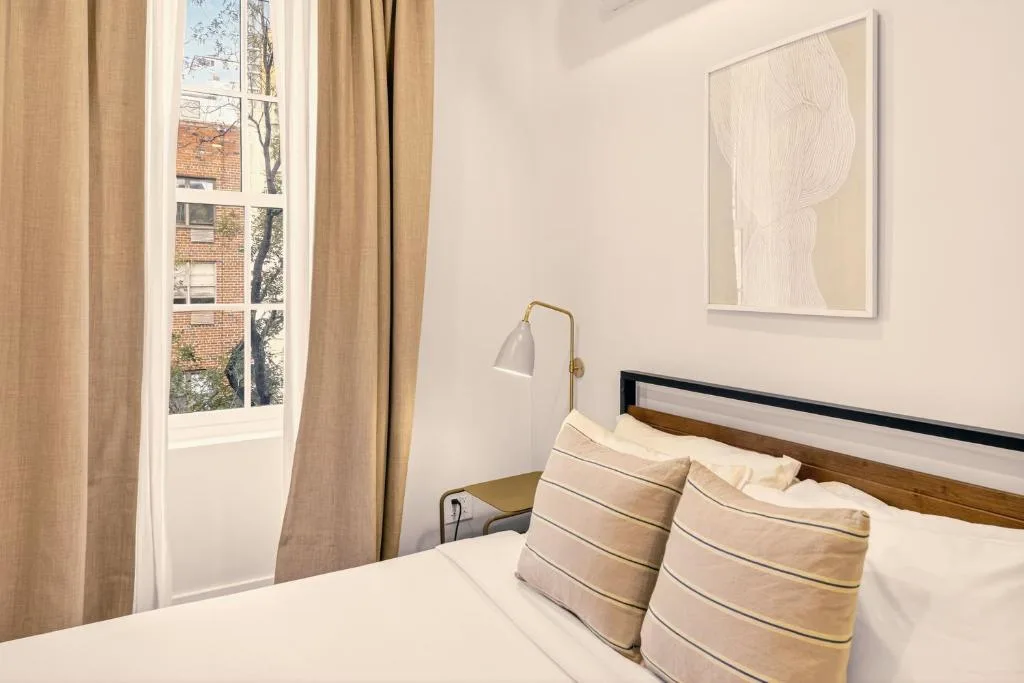 Minimalist bedroom with neutral tones, crisp white bedding and soft light through curtains in a cozy off-season stay.