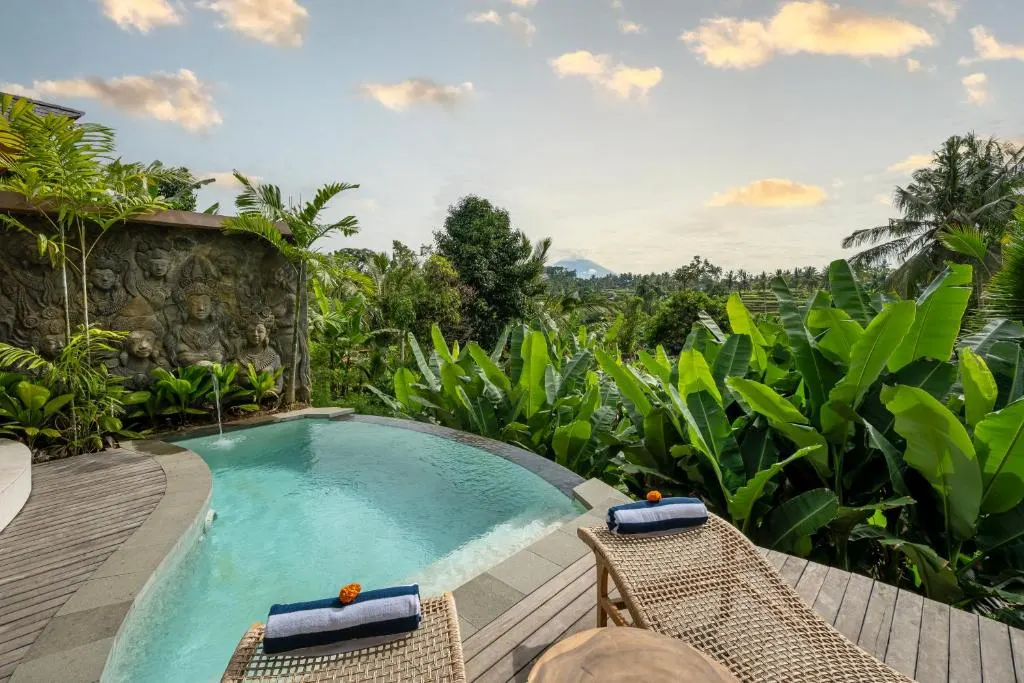 Off-season tropical resort with carved stone wall, empty loungers and infinity pool overlooking lush jungle.