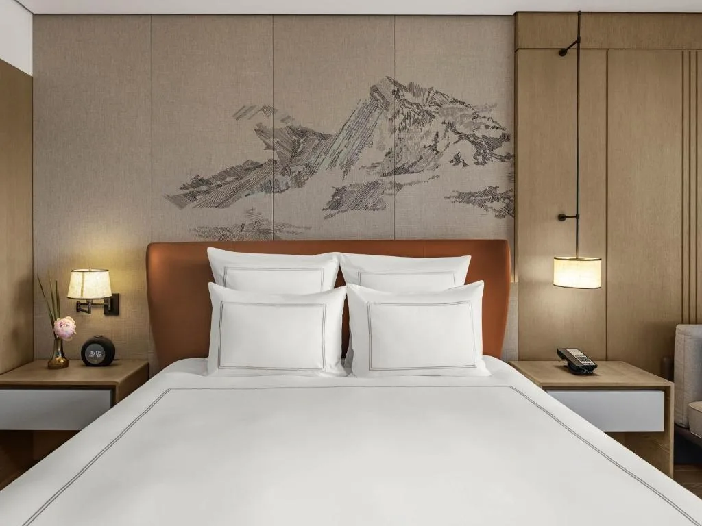 Off-season quiet retreat: modern hotel bedroom with crisp white linens, warm lamps, and mountain tapestry backdrop.