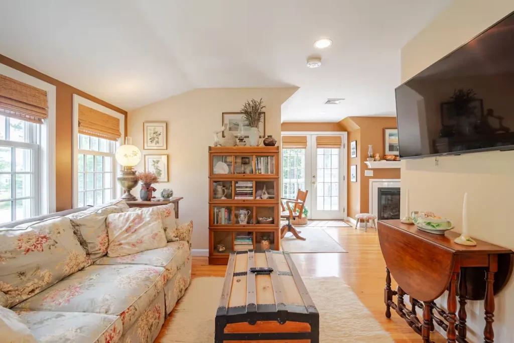 Cozy off-season vacation rental living room with floral sofa, rustic coffee trunk, bookshelves and soft natural light.
