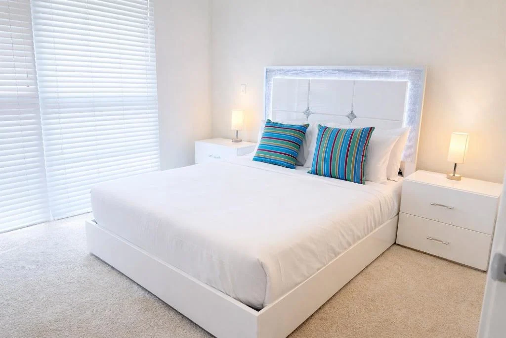 Modern guest bedroom with crisp white linens, striped blue accent pillows and natural light, serene off-season retreat