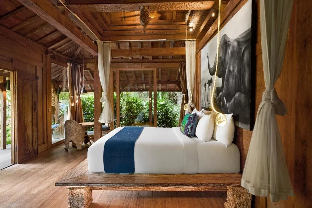 Empty wooden bungalow suite with canopy bed, soft pendant lights and lush garden views, serene off-season retreat