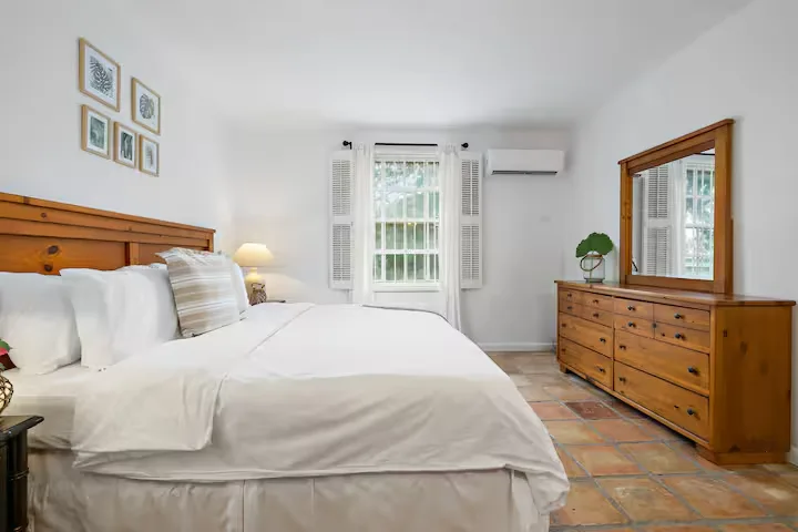 Bright airy vacation rental bedroom with rustic wood furniture and sunlit shutters, cozy off-season calm atmosphere.