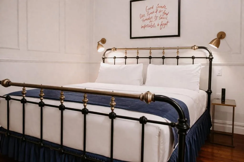 Cozy boutique hotel room with iron-framed bed, crisp white linens and navy runner, off-season travel vibe, quiet and peaceful
