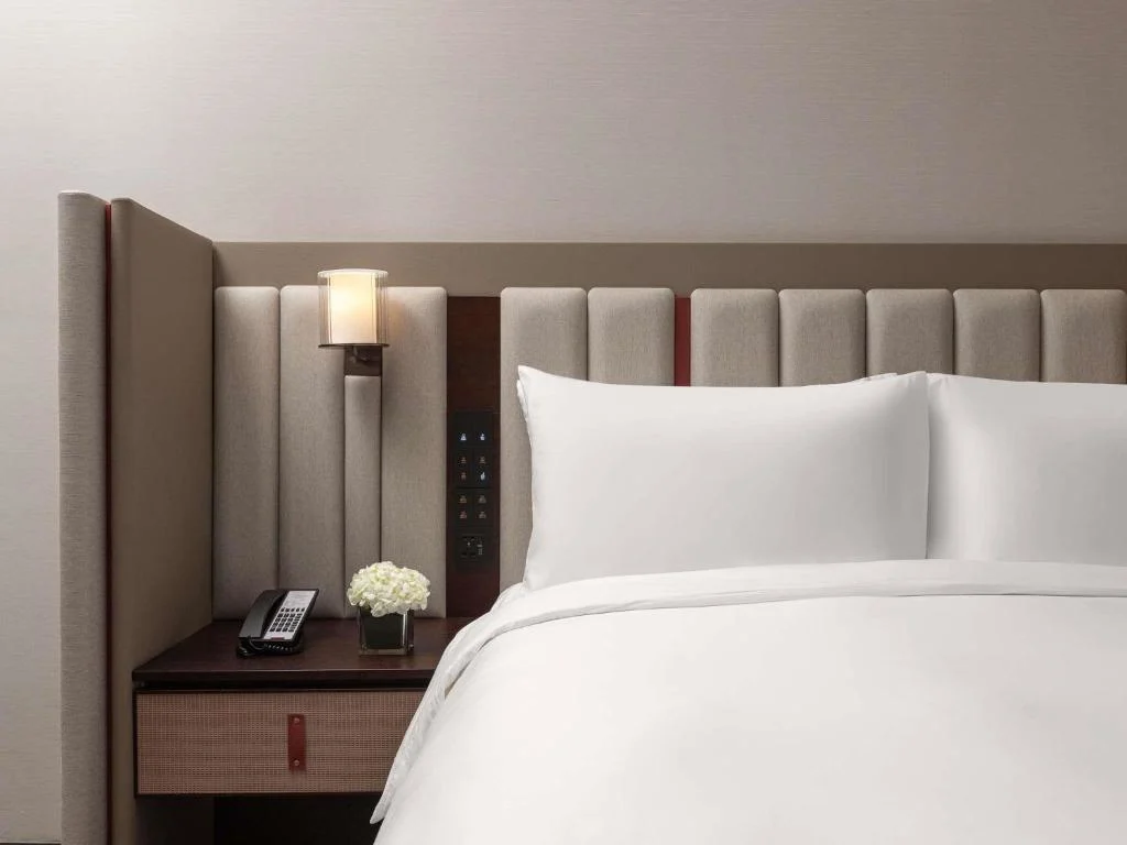 Serene off-season hotel room with plush white bed, padded headboard, bedside lamp and phone on wood side table