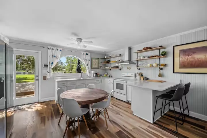 Cozy off-season vacation rental kitchen with round wood table, modern white chairs and peaceful yard view.