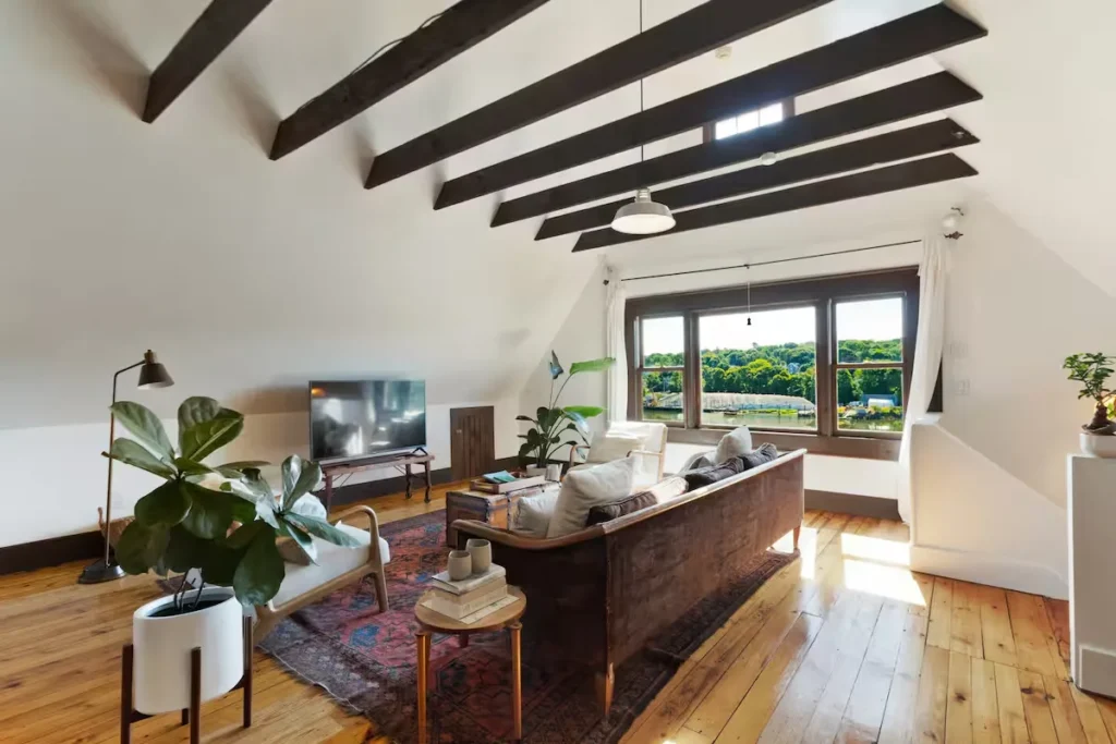 Cozy off-season loft living room with exposed wood beams, vintage sofa and serene river view, ideal quiet travel retreat