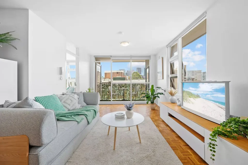 Modern vacation rental living room with balcony city view and TV beach scene, quiet off-season travel getaway.