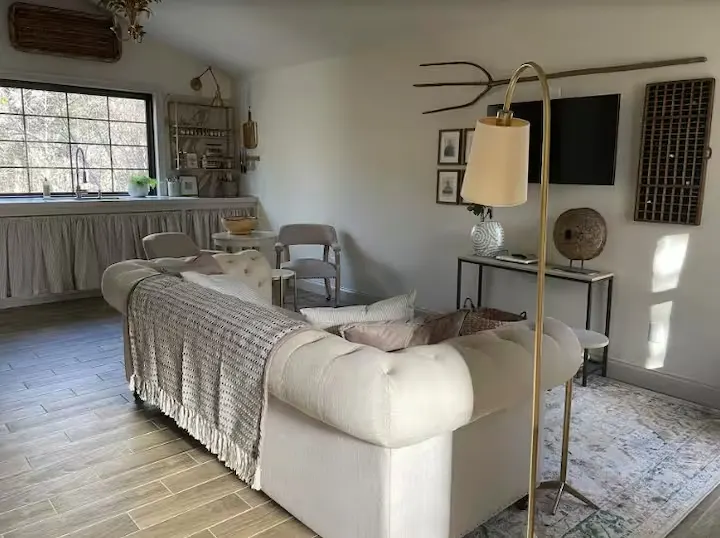 Cozy off-season rental living room with neutral sofa, rustic decor, soft sunlight through window, quiet retreat.