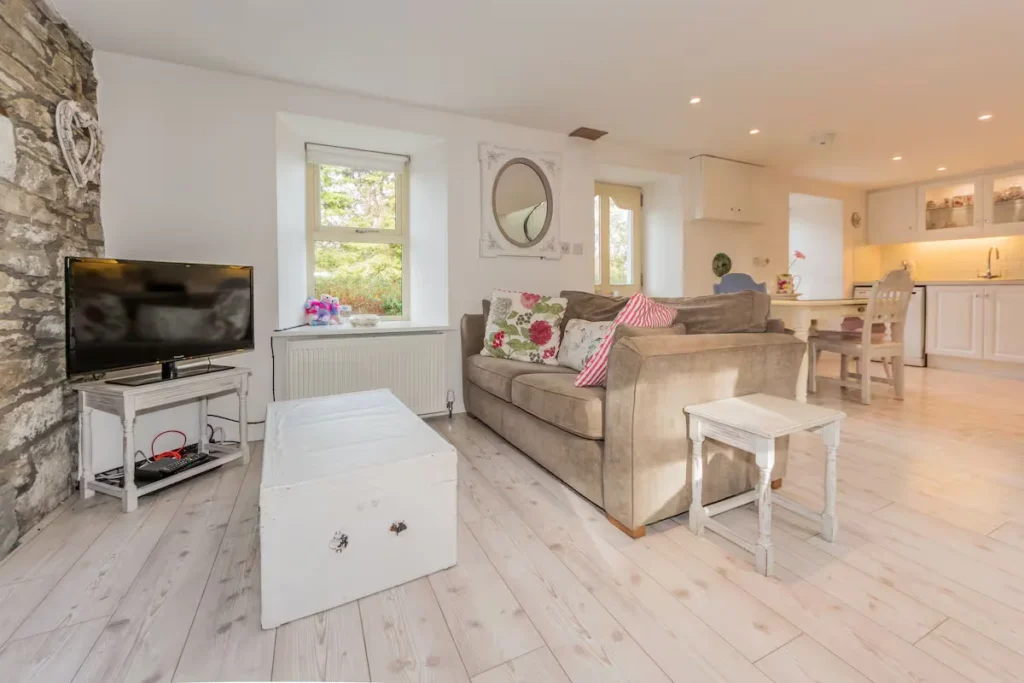Bright, cozy cottage living room with stone accent wall, plush sofa and kitchenette, a quiet off-season vacation retreat.