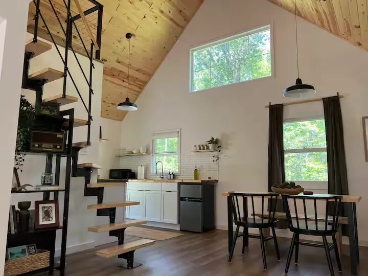 Quiet off-season cabin interior with wood-paneled vaulted ceiling, spiral stairs, open kitchen and forest views