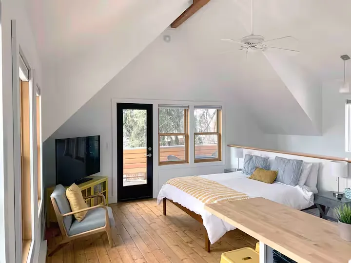 Cozy sunlit loft bedroom with vaulted ceiling, wood floors and balcony doors, ideal for a quiet off-season retreat.