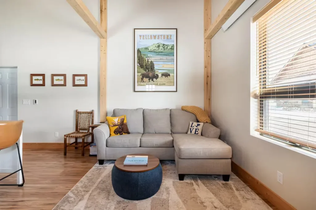 Cozy living room in an off-season vacation cabin with sectional sofa, wooden beams, nature wall art and warm light