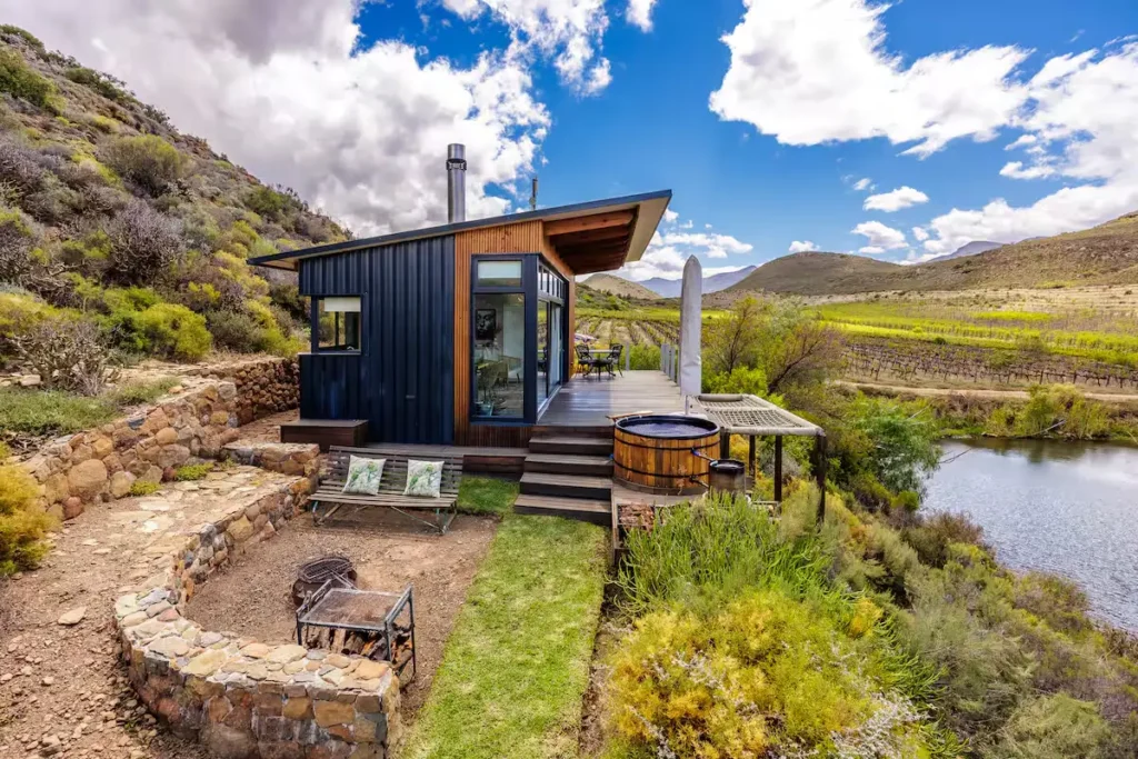 Modern hillside cabin above a quiet riverside vineyard in off-season, cloudy skies and empty outdoor lounge for serene escape