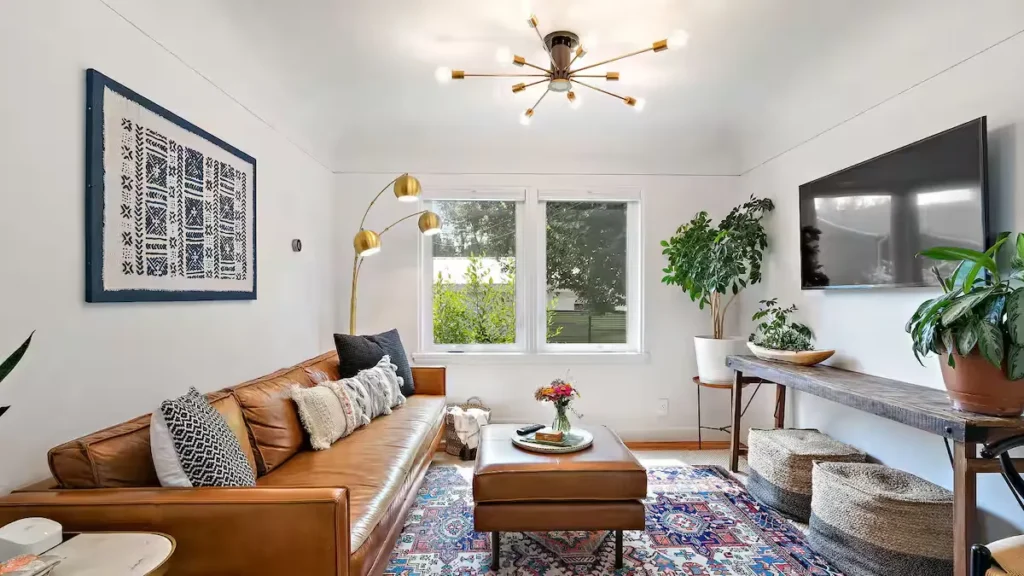 Quiet off-season vacation rental living room with leather sofa, patterned rug, potted plants and bright minimalist decor