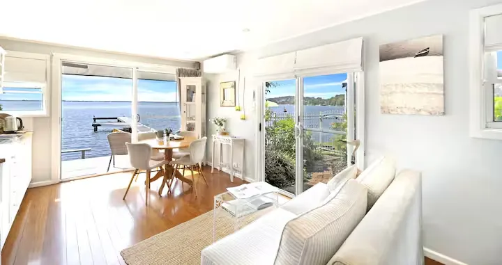 Bright lakeside retreat interior with cozy living and dining space, panoramic water view and empty dock in serene off-season.