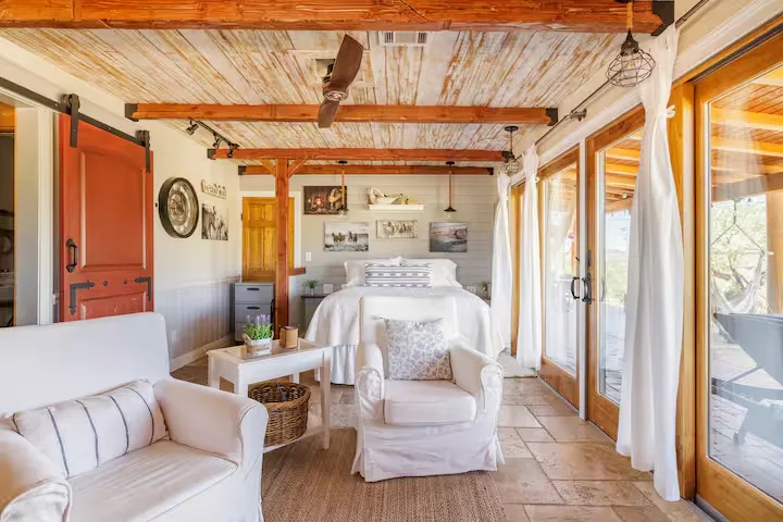 Cozy rustic cabin interior with white linens, wooden beams and glass doors opening to a quiet off-season getaway retreat.