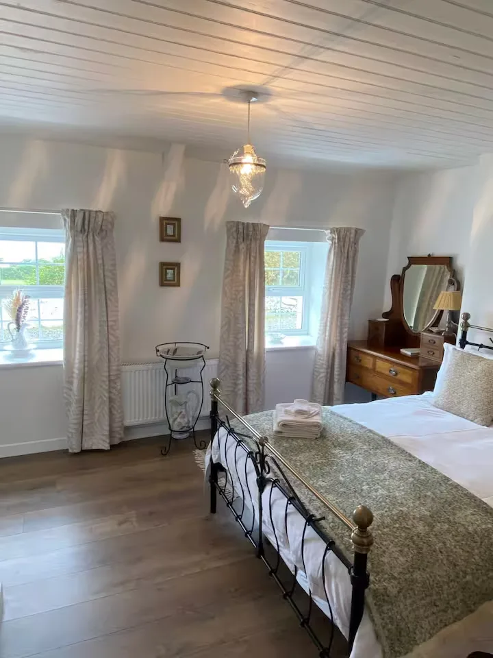 Cozy countryside guest room for off-season getaway with iron bed, green throw, wooden floors and soft natural light.