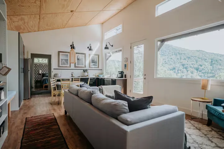 Cozy cabin interior with sofa, kitchen and large windows overlooking quiet forested hillside in off-season.