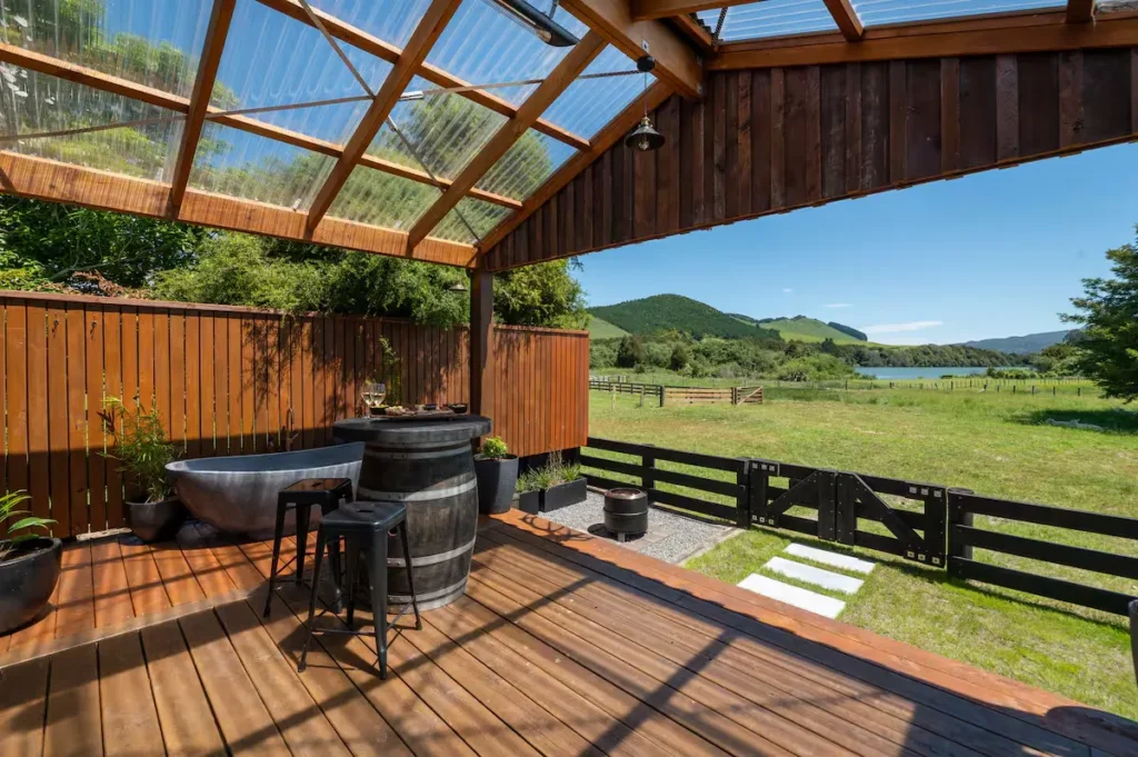 Off-season travel: rustic covered deck with barrel table and wine glasses overlooking quiet pasture and hills by a lake