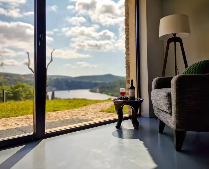 Cozy off-season lakeside retreat: armchair by glass doors opening to quiet lake and rolling hills, wine awaits.