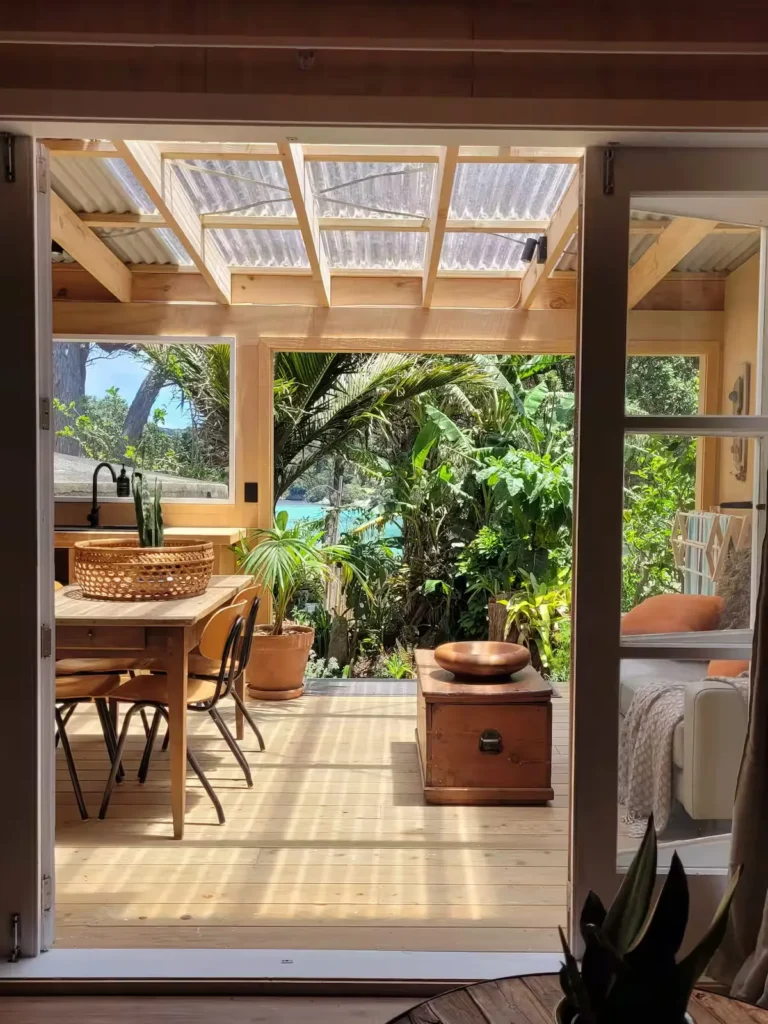 Cozy wooden deck of a tropical cabin opening onto lush greenery and a serene off-season beach.