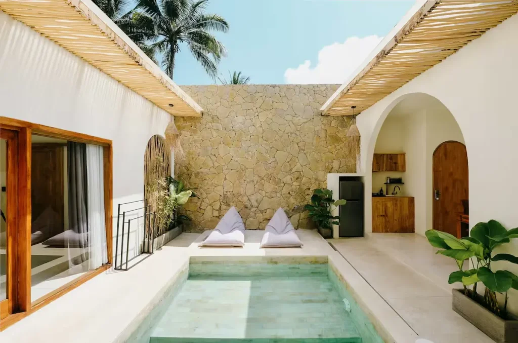 Serene off-season tropical villa courtyard with private plunge pool, loungers, stone wall and palm shade