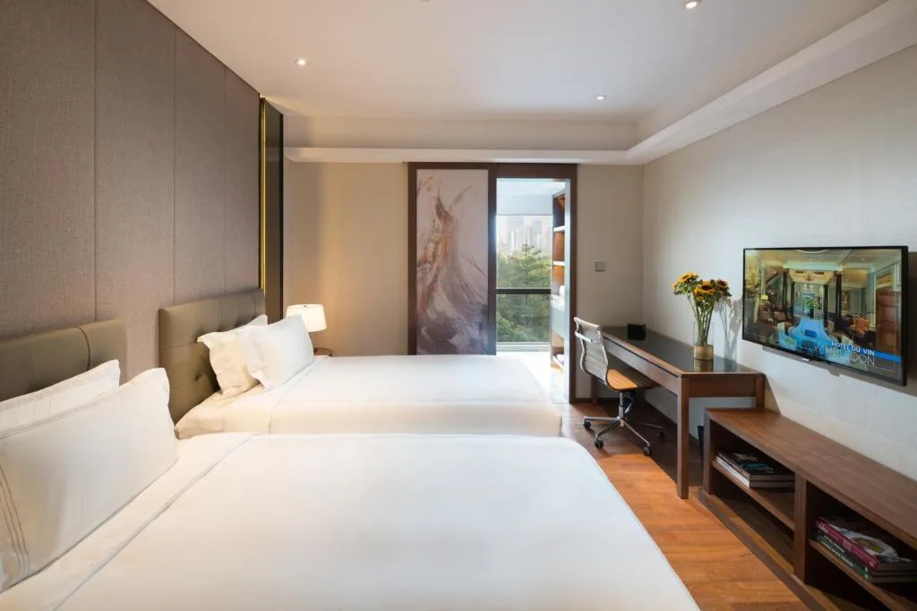 Serene off-season modern hotel room with two beds, work desk and balcony overlooking quiet city greenery.