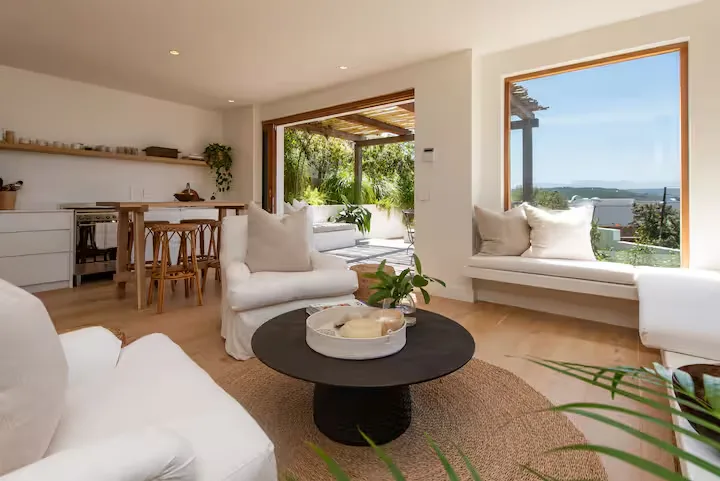 Serene off-season coastal villa living room with white sofas, wooden accents and open doors to a quiet outdoor patio.