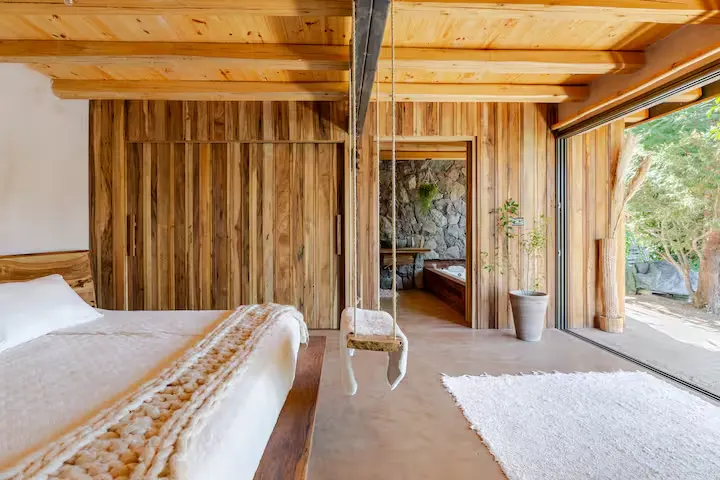 Cozy rustic cabin interior with wooden beams, swing seat and open wall to lush garden in off-season travel retreat