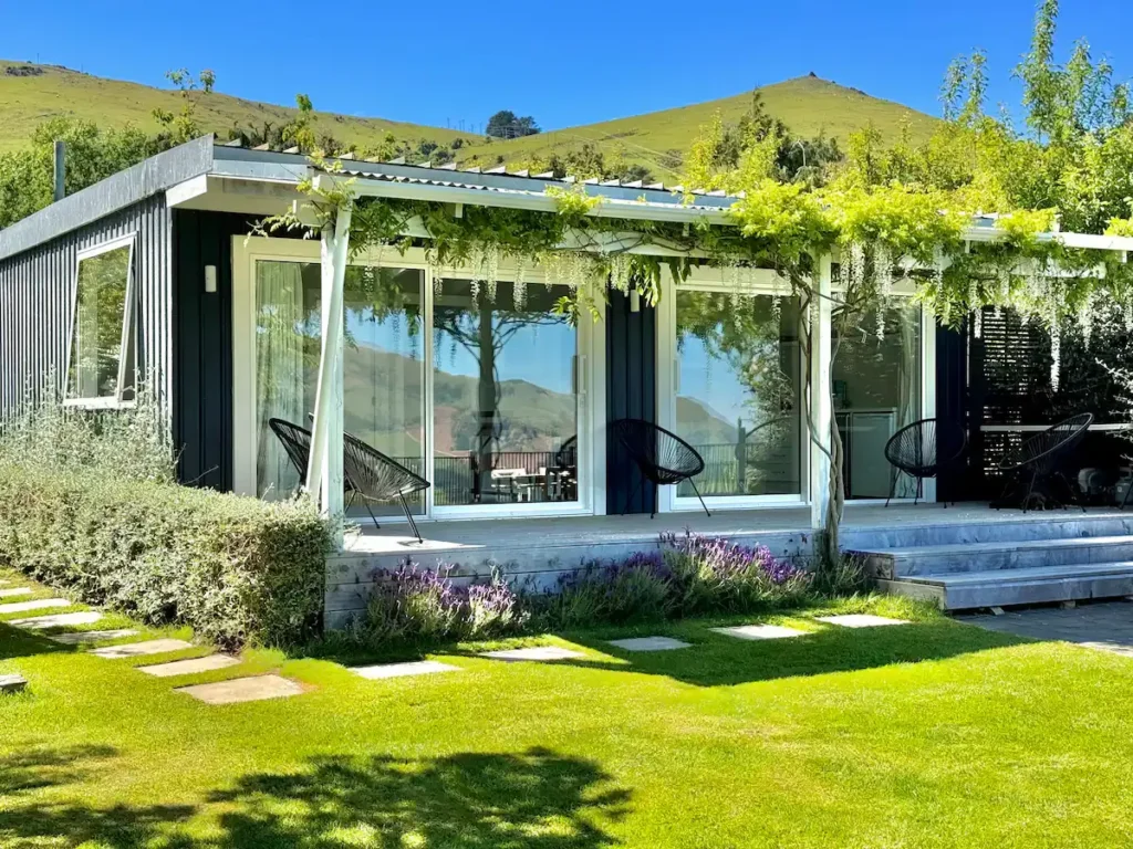 Off-season vacation cabin patio with empty lounge chairs, lush green lawn and rolling hills under clear blue sky