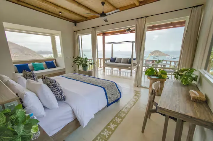 Bright off-season seaside resort suite with king bed, open-air terrace seating and panoramic ocean view over quiet islands.