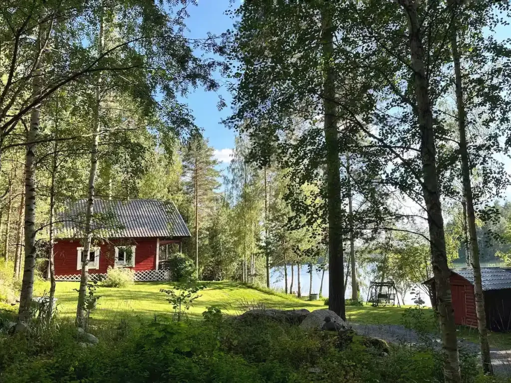 Secluded red cabin nestled among birch trees by a quiet lake, evoking a peaceful off-season lakeside forest retreat.