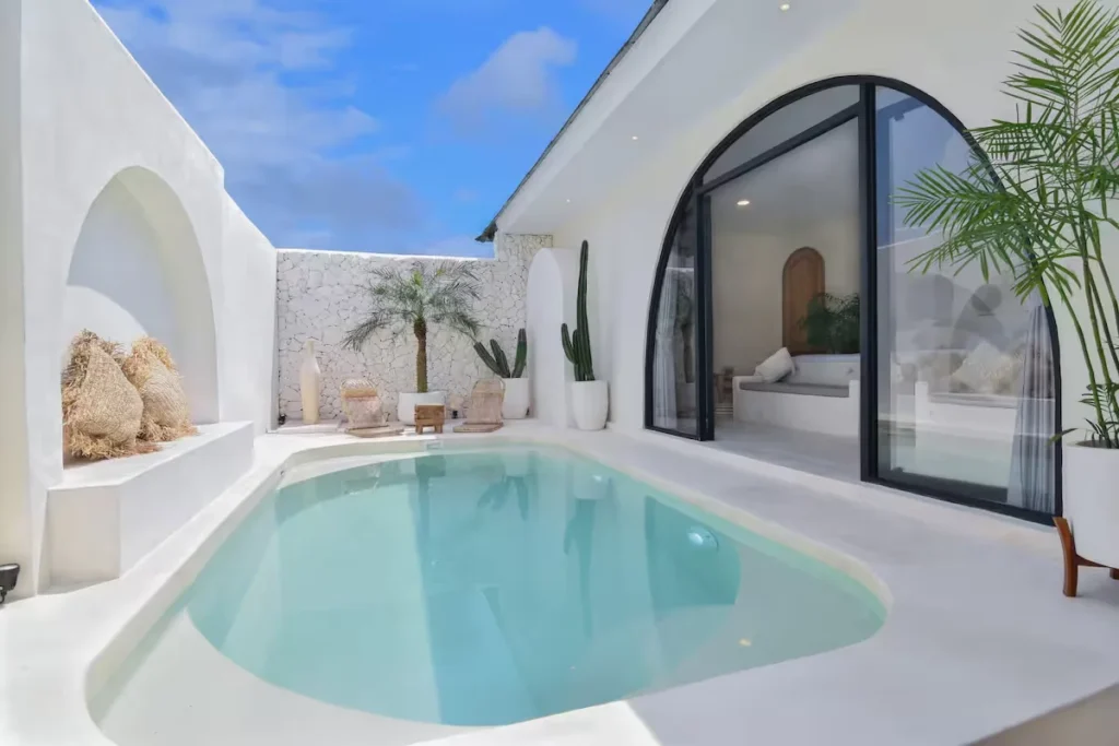 Secluded white-walled courtyard with empty turquoise pool, wicker chairs and potted palms in Mediterranean off-season villa.
