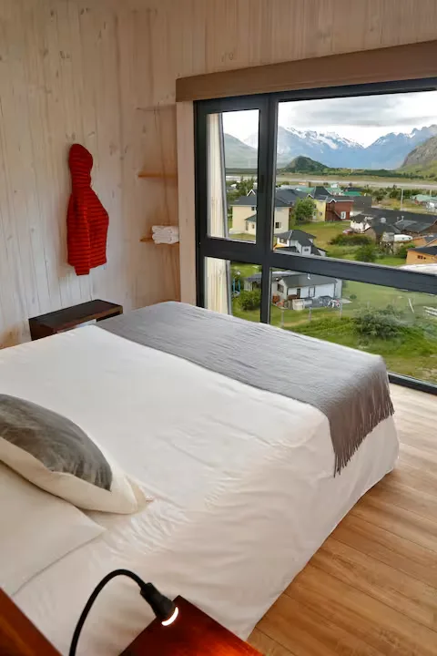 Cozy wooden bedroom with fjord view overlooking a quiet mountain village under cloudy skies in off-season calm.