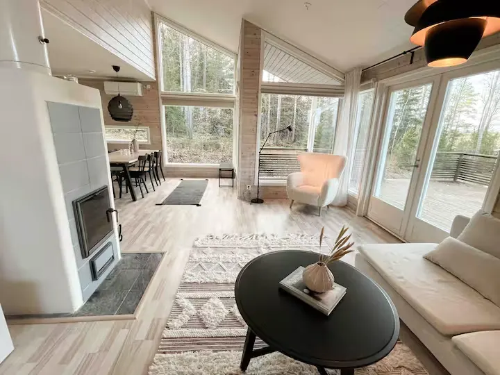 Cozy off-season forest cabin interior with wood walls, large windows overlooking bare trees and a simple dining nook.