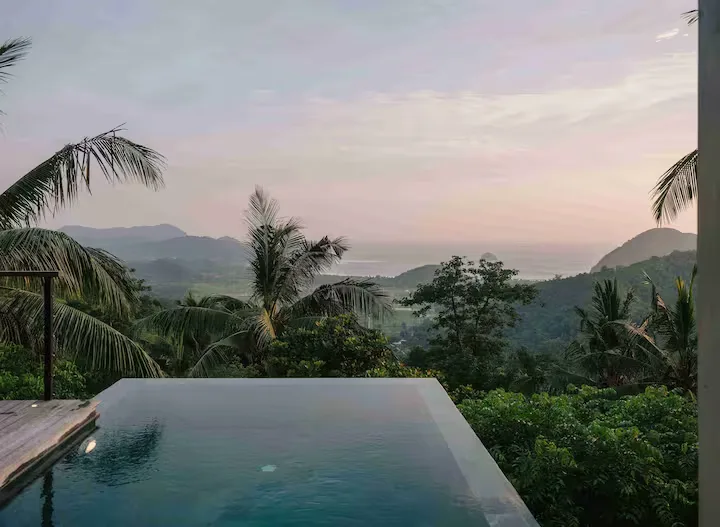Empty infinity pool overlooking misty hills and calm sea at sunrise, off-season serenity in palm-fringed getaway