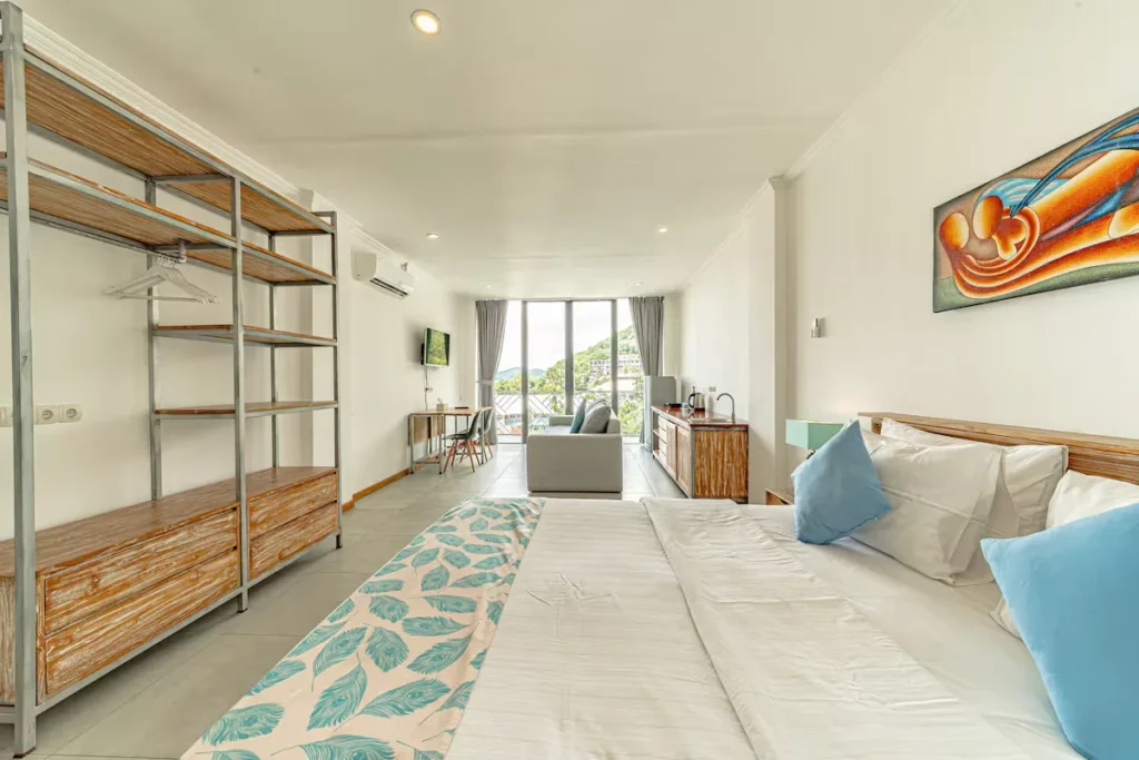 Bright modern hotel room with king bed, open closet and balcony overlooking a quiet hillside—ideal off-season retreat.