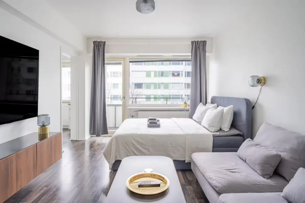 Bright modern studio apartment interior with bed, sofa and balcony view, quiet off-season travel rental vibe.