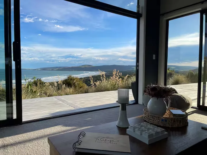 Modern coastal retreat with open glass doors leading to a quiet deck and off-season beach view over rolling hills.