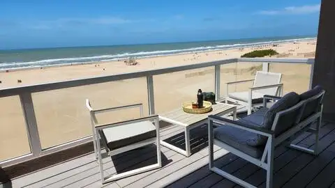 Off-season beachfront deck with modern lounge chairs and wine bottle overlooking a deserted sandy beach and calm ocean
