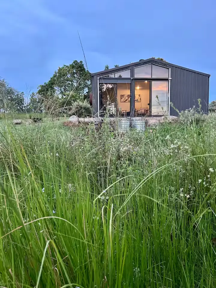 Modern glass-front cabin at dusk amid tall grasses in a serene off-season countryside retreat