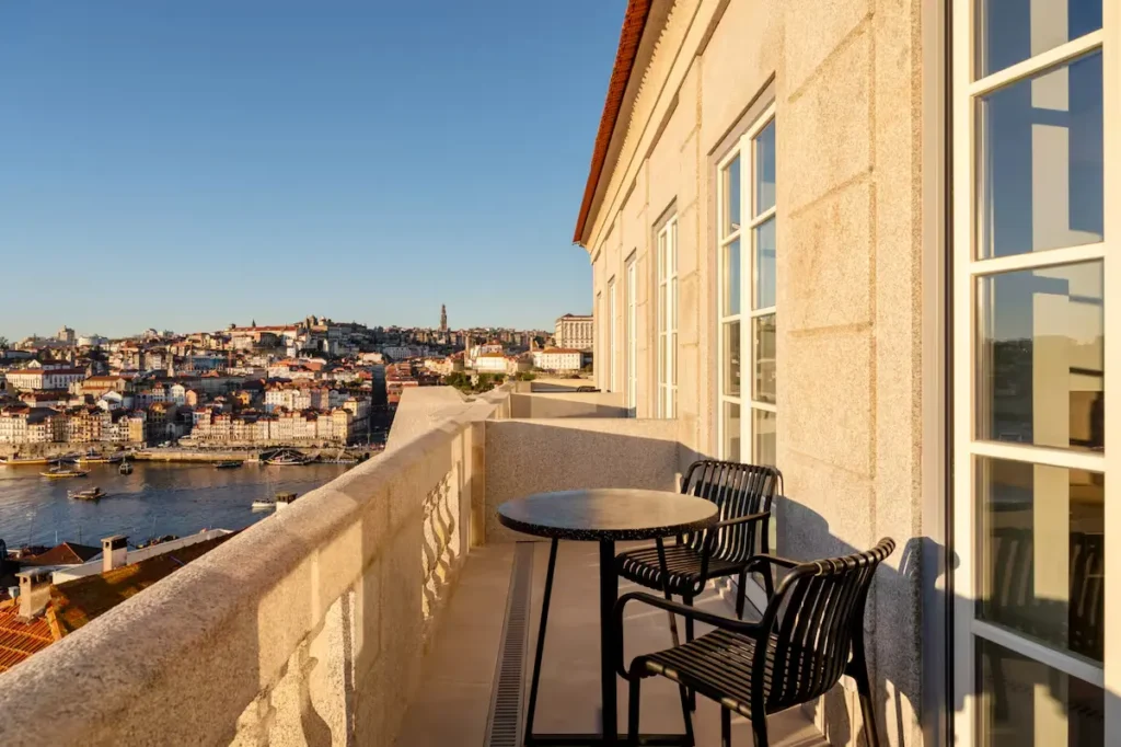 Empty balcony with table and chairs overlooking Porto’s Douro River in off-season golden light.