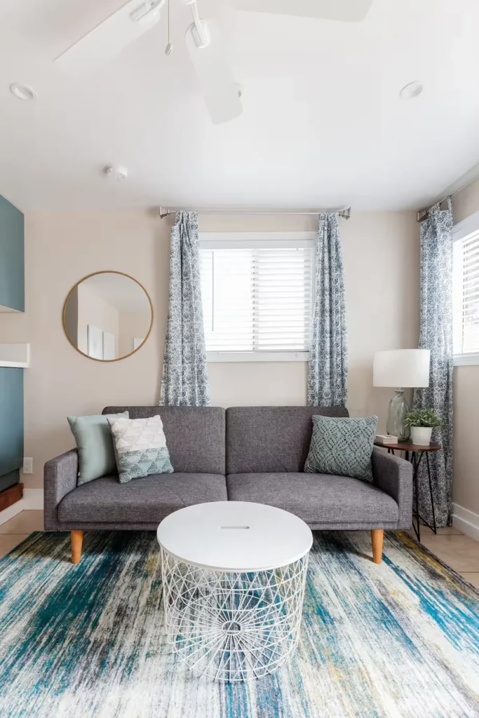 Quiet coastal rental living room off-season with gray sofa, patterned rug and soft natural light.