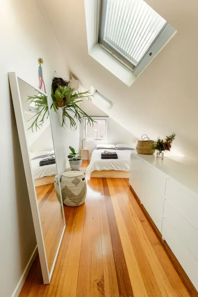 Sunlit attic bedroom with skylight, wooden floors, indoor plants and crisp linens, a serene off-season travel retreat