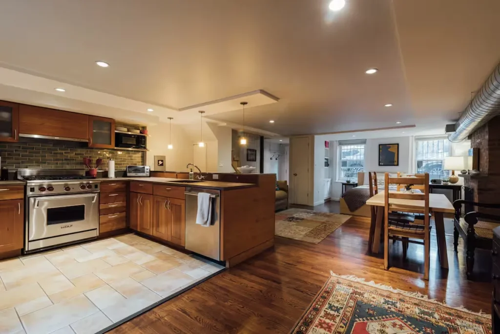 Cozy off-season vacation rental interior with empty open-plan kitchen and dining area, warm wood tones and ambient lighting.